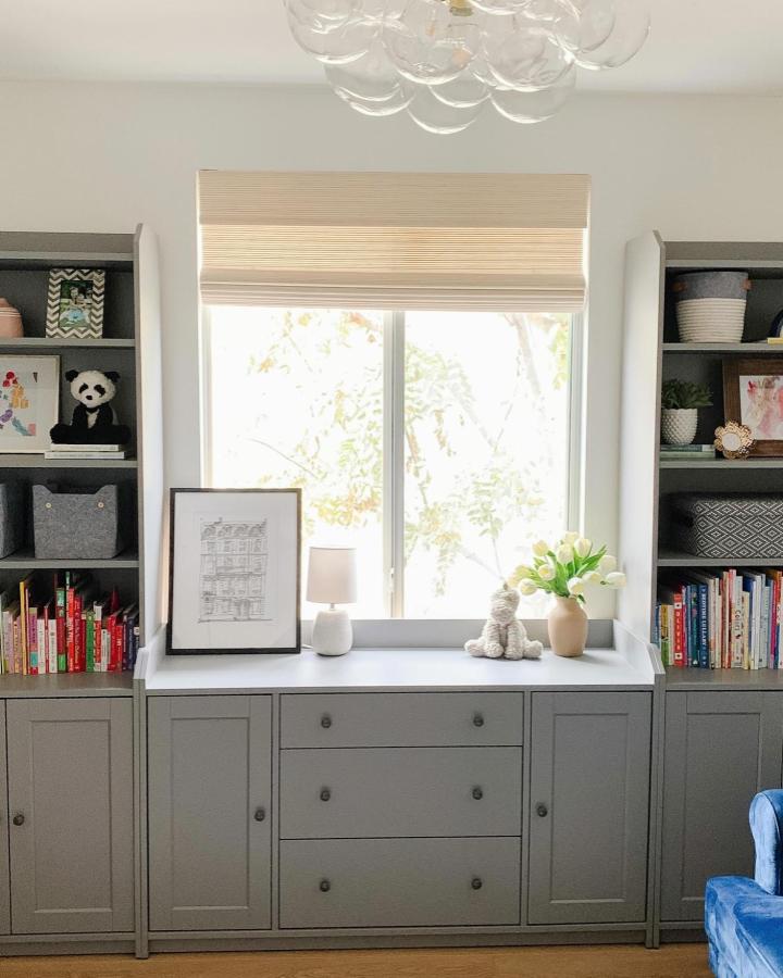 Gray painted built-in storage cabinets and shelves with books and decor by @stephaniecameroninteriors featuring custom Ikea furniture modifications and layered design.