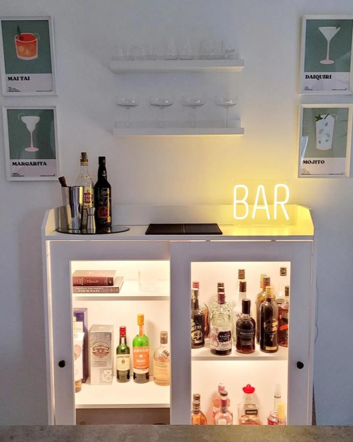 White minimalist bar cabinet with built-in lighting and glass shelves by @burns_dukeswood_home brightening a home cocktail setup with neon sign.