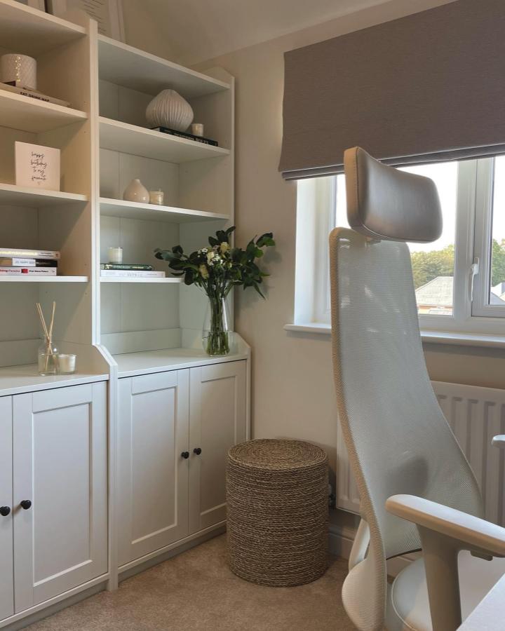 White minimalist shelving unit with natural woven stool and taupe window shade in cozy home office space from @houseonthegroves. Calm, stylish, and inviting.