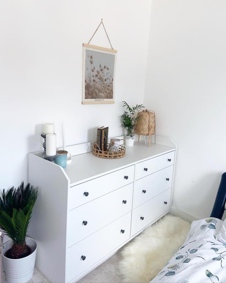 White minimalist dresser with black knobs and natural rattan accents in bright bedroom from @thefarajhome. Cozy, clean, and stylish storage solution.