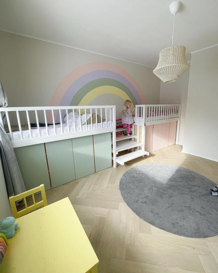 Pastel painted wood storage doors under white loft beds by @villakotila in kids room with rainbow wall mural. Soft matte finish colors and custom compartments.