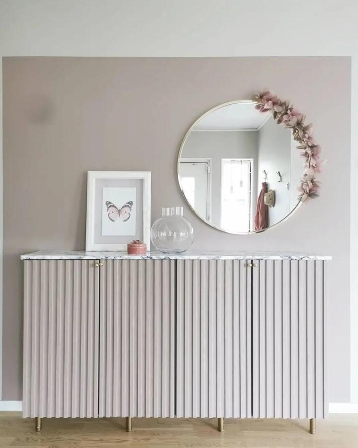 Blush fluted panel storage cabinet with brass accents and marble top from @rebeccashem in a modern living space.