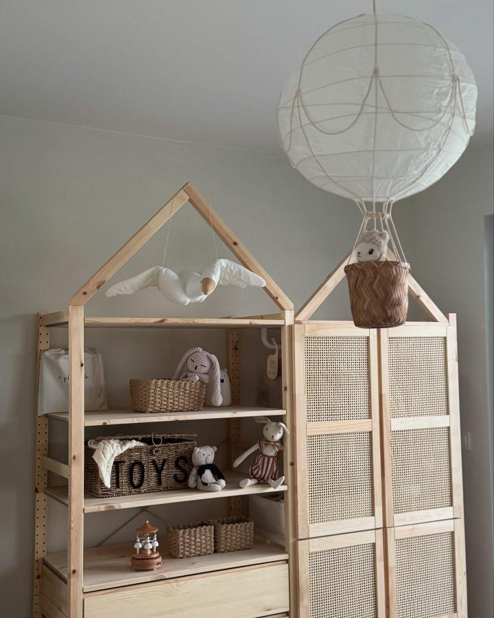 Natural pine wood shelving with rattan doors and playful house frame from @kristyna.living. Cozy kids storage with textured baskets and toys.