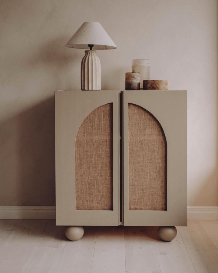 Muted beige wooden cabinet with fabric door panels and rounded feet from @sanna.emelie styled with ceramics and lamp in neutral tones. Elegant storage makeover.
