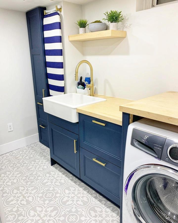 Navy blue cabinets with maple countertop and gold hardware in ikea laundry room storage from @_the_woodworkers_wife. Includes floating maple shelf and ironing board storage.