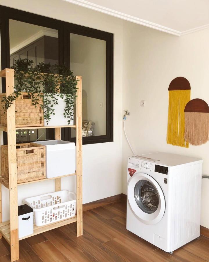 Natural wood shelving unit with wicker baskets and white storage boxes from @deregenbogenhaus in a bright laundry room with a washing machine.