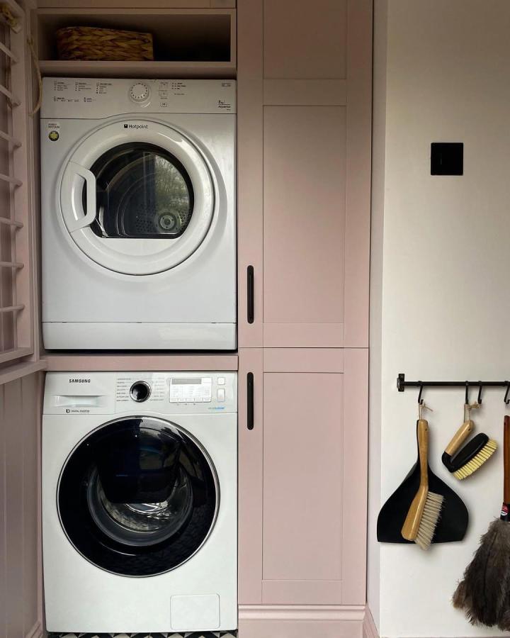 Soft pink modern cabinets laundry nook from @mabelinthehouse with stacked washer dryer and black hardware. Simple functional setup.