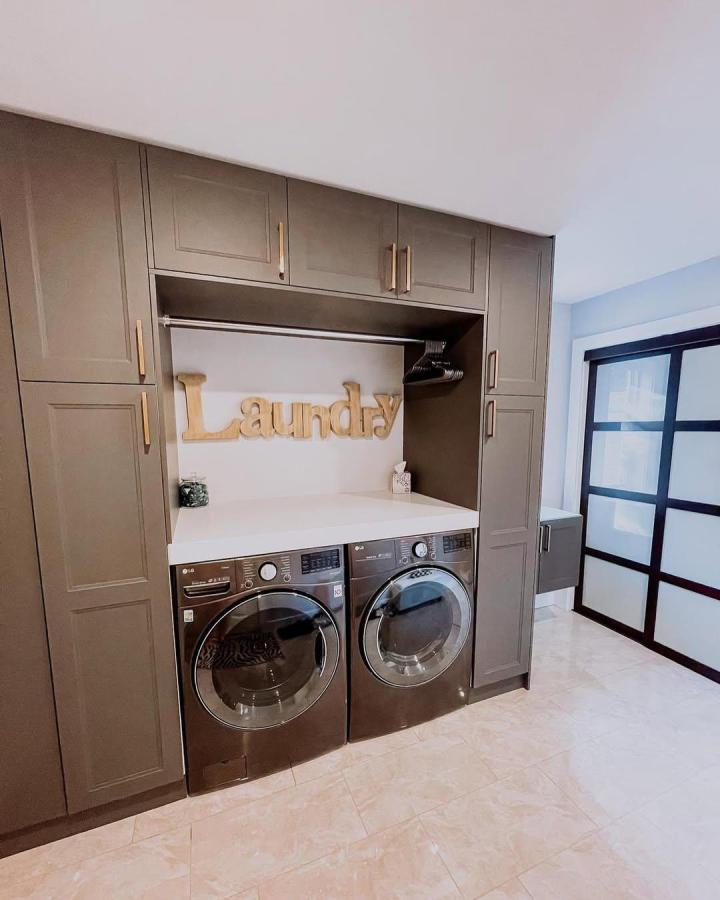 Taupe Ikea AXSTAD cabinets in laundry room storage from @modahomes featuring washer, dryer, brass hardware, and built-in hanging rod.