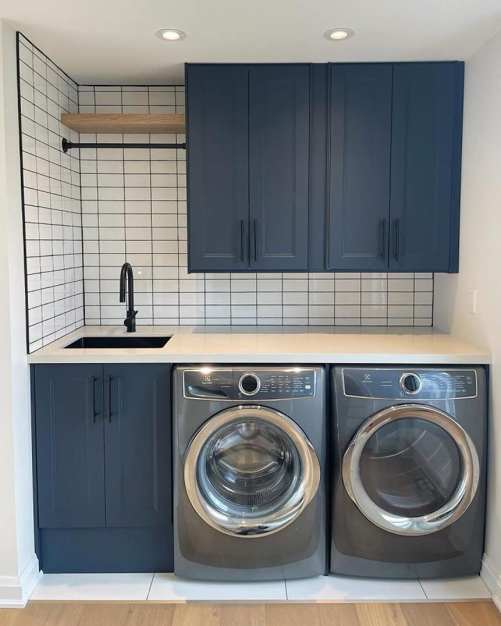 Navy blue Ikea cabinets laundry room storage with black accents and wood shelf from @jjlegacycontracting. Modern and tidy design.