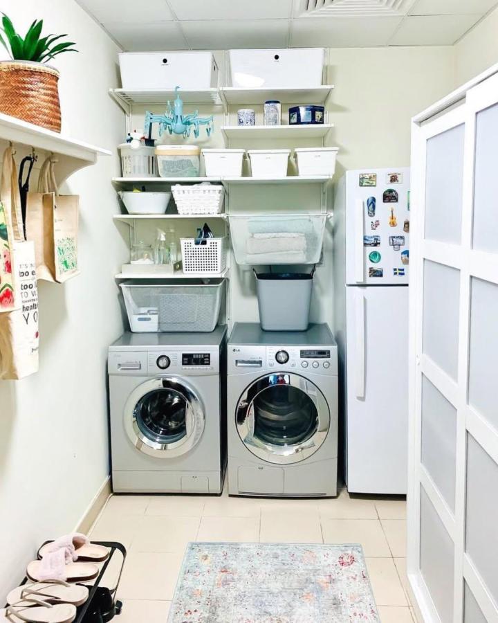 Silver washer and dryer with white IKEA vertical shelving unit and storage bins for ikea laundry room storage by @cleartheclutterdxb showing organized laundry space.