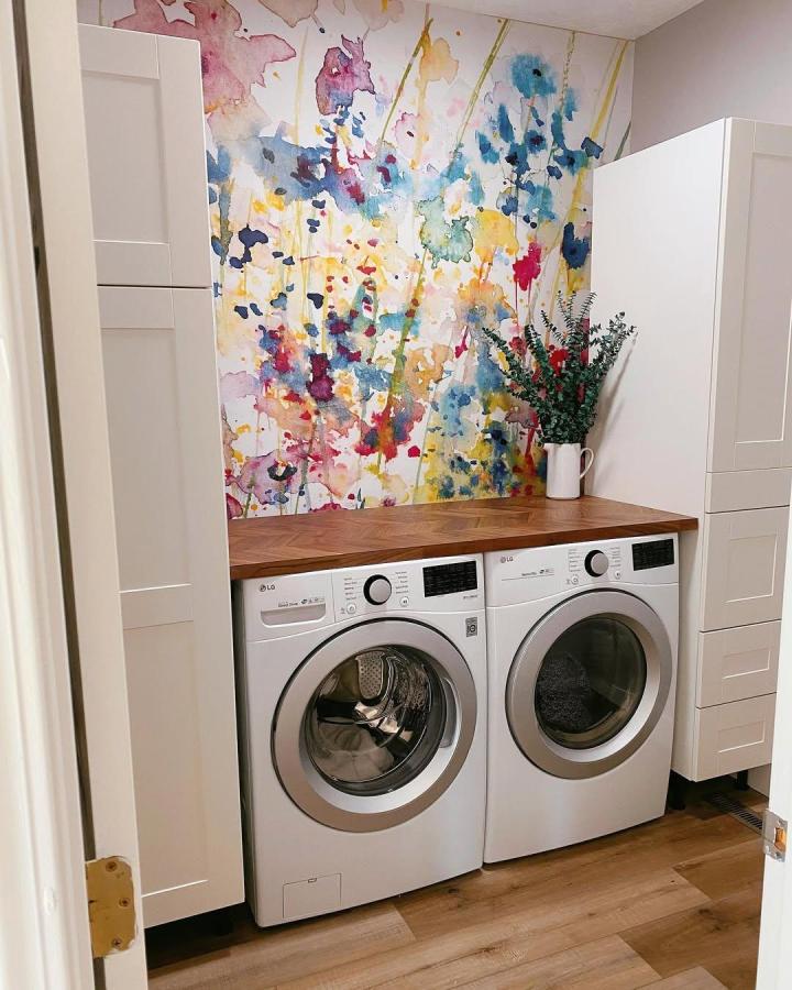White Ikea cabinets with wood folding counter in laundry room from @poojakotz. Colorful watercolor wall brightens ikea laundry room storage space.