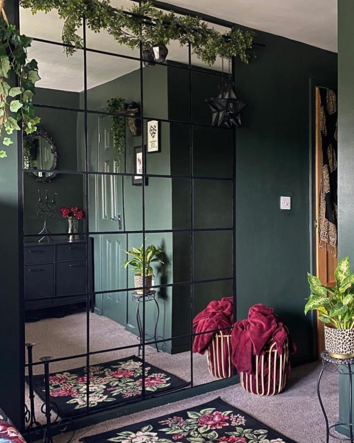Dark green grid style ikea mirror wall in a cozy room from @shade.of.dark with black framing and floral accents.