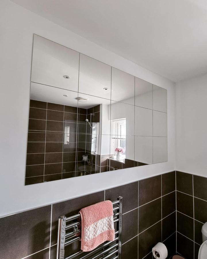 Brown tiled bathroom with modular square mirror panels from @ourlifeatcarnaby reflecting a bright shower space and cozy towel rack.