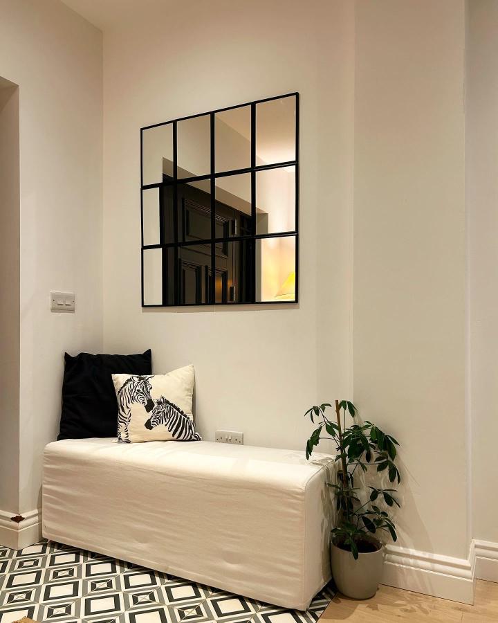 Black framed segmented wall mirror in cozy entryway from @gort_na_gainimhe_house with modern geometric floor tiles and soft bench.