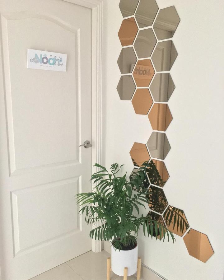 Bronze and clear honeycomb shaped reflective wall panels by @that_fresh_look arranged vertically near a white door and plant.