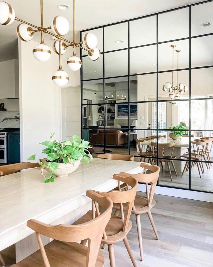 Light wood dining area with black framed reflective panels from @roomhomestyling. Industrial style adds depth and brightness.