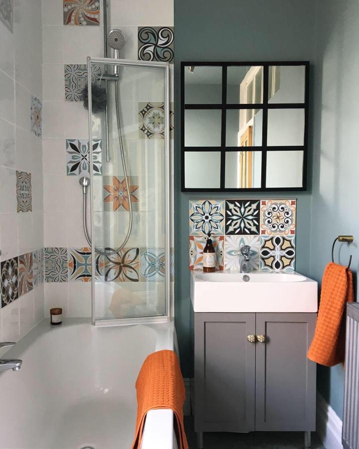 Black framed windowpane style mirror in small bathroom by @gingerhearts with colorful patterned tile backsplash and gray vanity. Brightens space.
