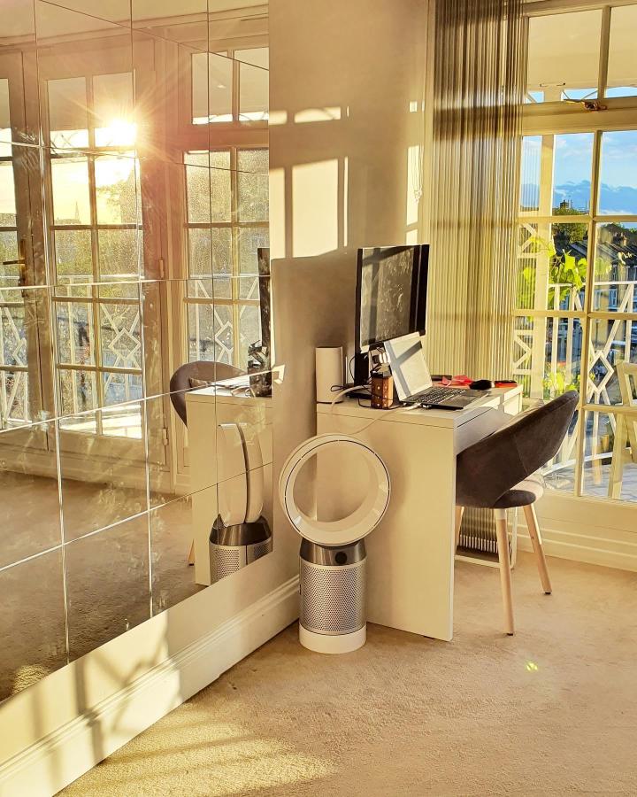 Bright reflective grid Ikea mirror wall in home office with beige carpet and minimalist furniture from @shimashome reflecting sunlight and window details.