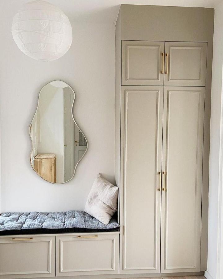 Beige custom cabinet mudroom with cushioned bench and brass handles by @by_sachse featuring METOD and PLATSA elements. Contemporary and inviting entryway.