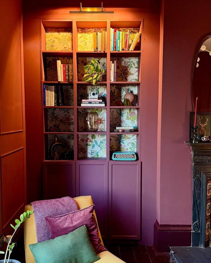 Terracotta painted Billy bookcase with floral wallpaper backdrop and cozy colorful cushions from @baysmac showcasing botanical charm.