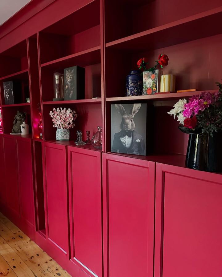 Cranberry red painted built-in style bookcase with matte finish and decorative trim from @ourbarncottage showing cozy display and storage details.
