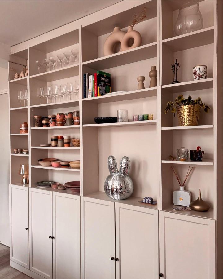 Neutral beige painted Billy bookcase with mixed ceramics, glassware, and decorative accents from @leighsliving styled with cozy matte finish and black knobs.
