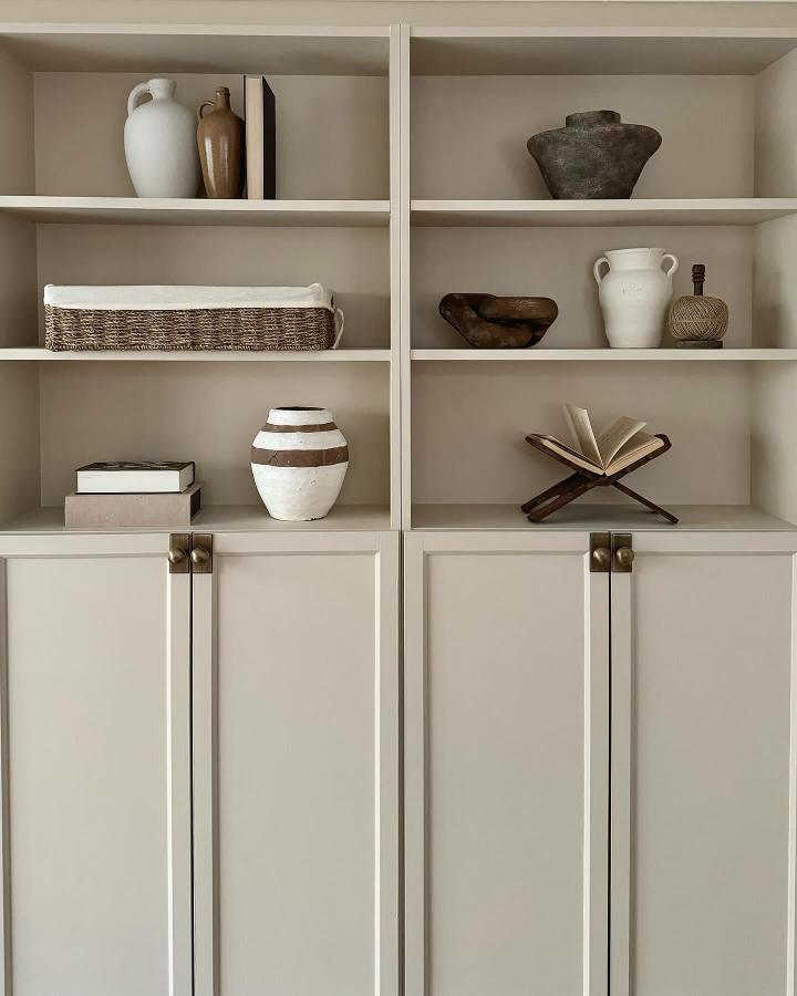 Beige painted wooden bookcases with brass handles and natural ceramic decor by @_homeofvictoria showing calm and minimal styling.