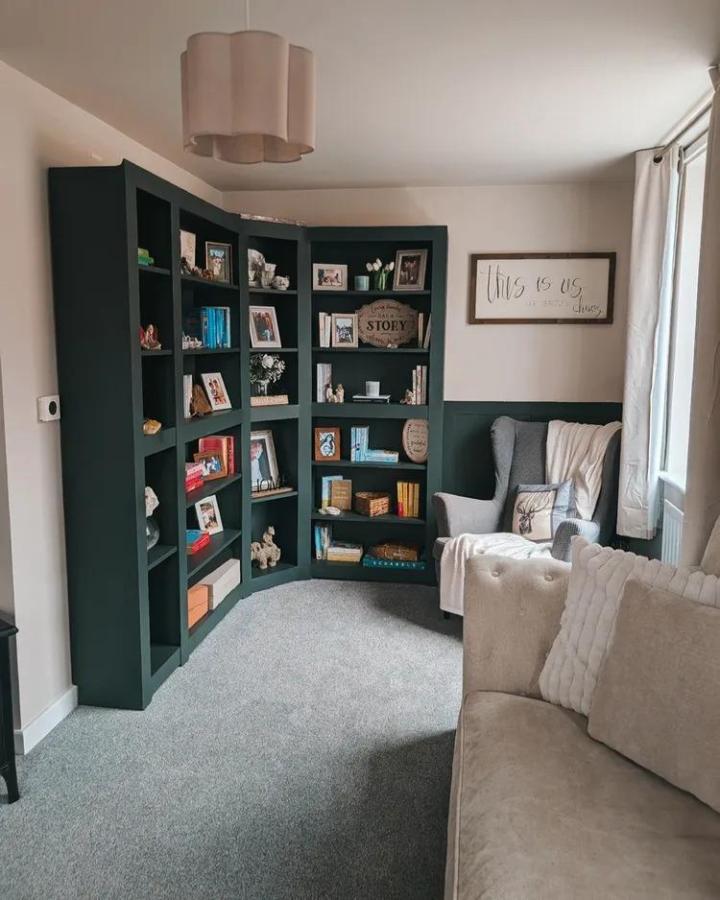 Deep forest green painted corner bookcase with books and decor from @thecornerofnewbuildtoforever in cozy living room.