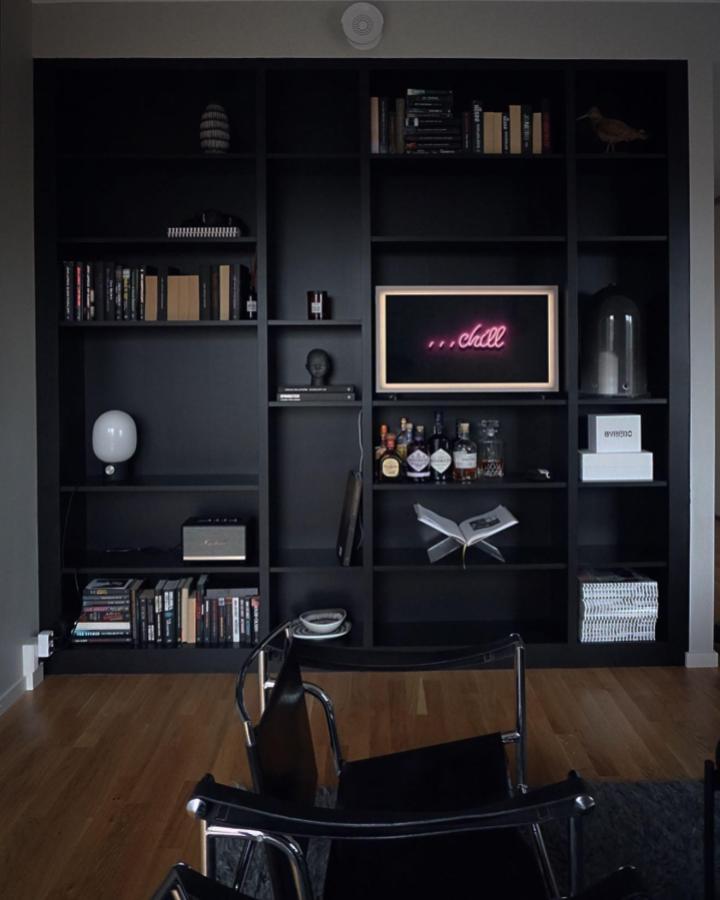 Matte black painted bookcase with neon pink light and decorative elements in modern living room by @ragnegardlinne minimalist moody style.