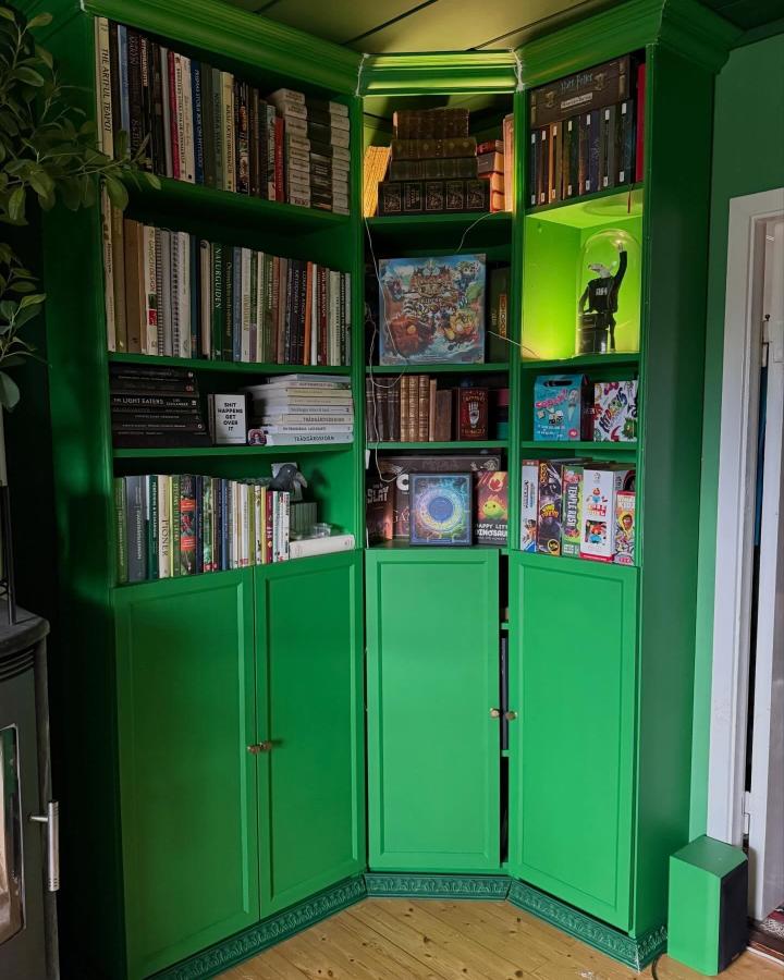 Bright green corner bookshelf with crown molding and mixed storage from @kimsywhimsycraft. Bold painted makeover with open and closed shelves storing books and games.