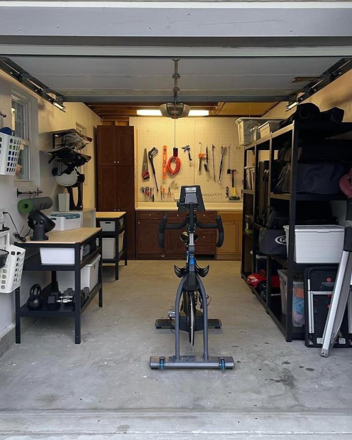 Dark wood cabinets and black metal shelving garage storage from @aclearmindorganizer. Organized tools and exercise bike at center.