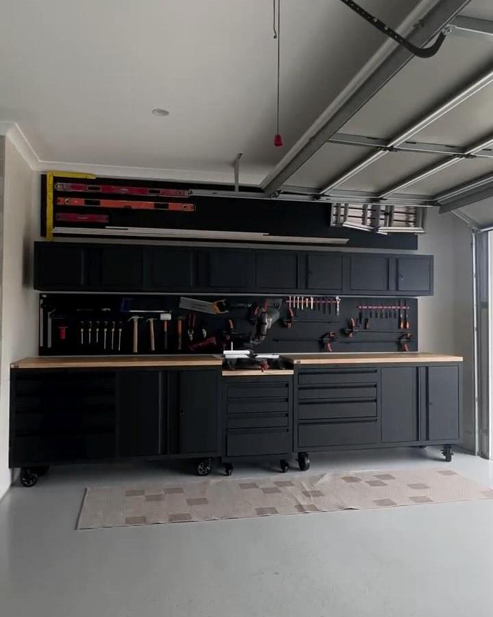 Black modular garage cabinetry with wood tops and tool organization by @ourcountrycoastalhome. Modern, mobile, and sleek workspace design.