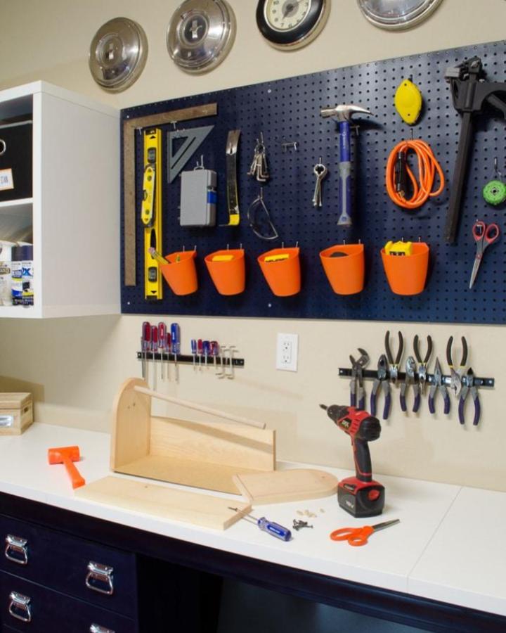 Bright orange buckets on black pegboard with IKEA KALLAX units in a garage workspace from Polished Habitat Tools hung neatly and accessible.