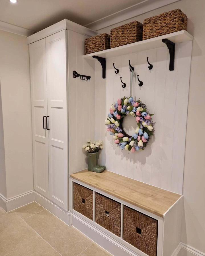 Natural woven basket bench and white wood panel entryway from @ourhomeinfyfield with hooks and floral wreath accents. Bright and organized storage space.
