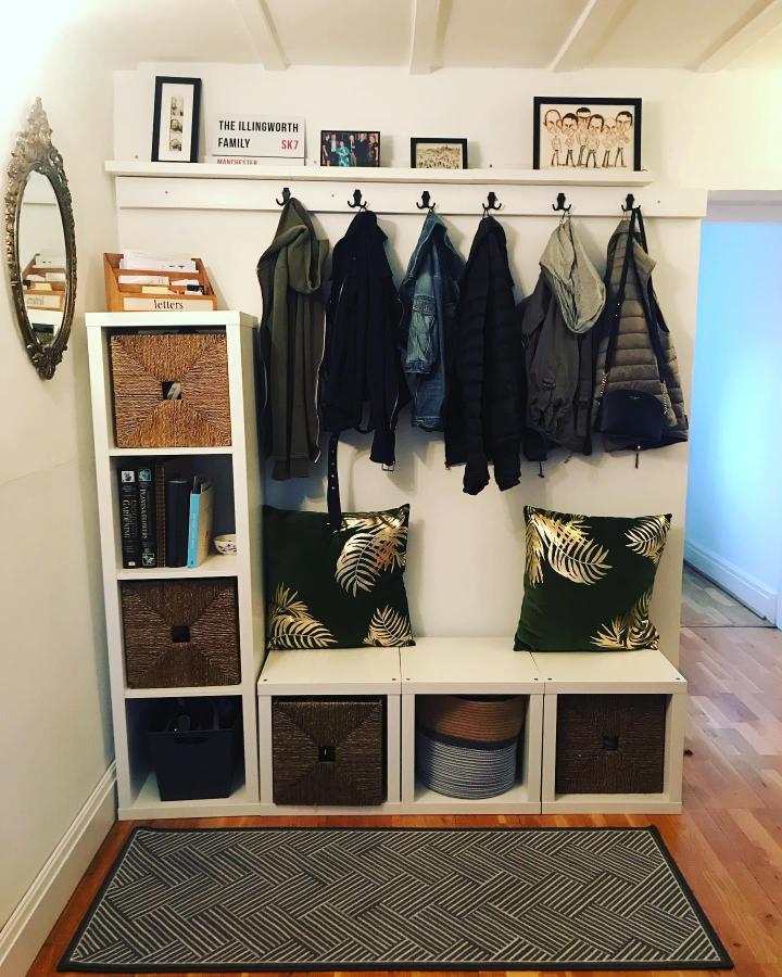 White Ikea Kallax storage bench with woven baskets and green leaf cushions in cozy entryway space by @the_weavers_cottage. Organized and functional.