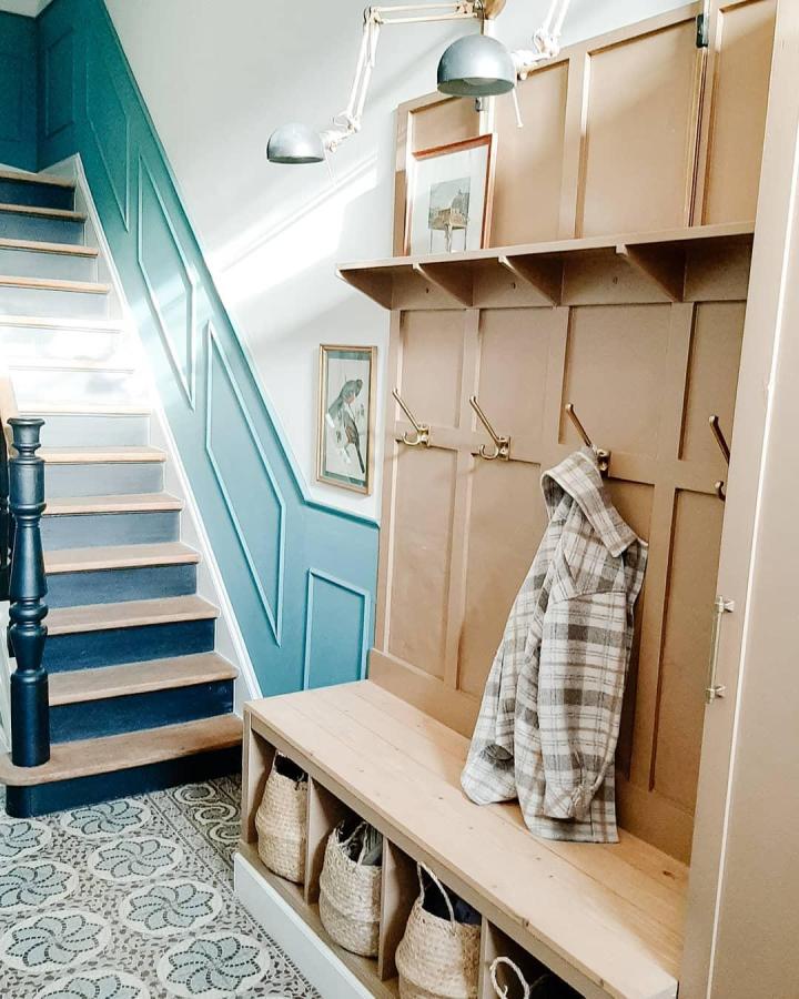 Light brown wooden bench with woven baskets and brass hooks in an entryway by @cas_par_k. Cozy and organized space.