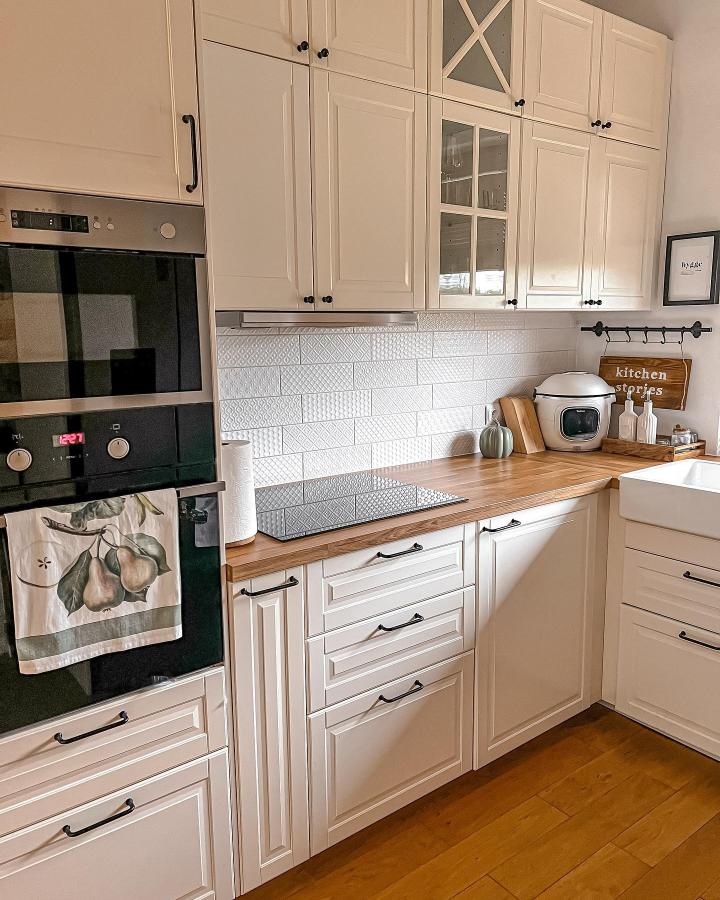 White shaker style kitchen cabinets with black handles and textured white tile backsplash from @stowidokow.home showing creative kitchen storage solution.