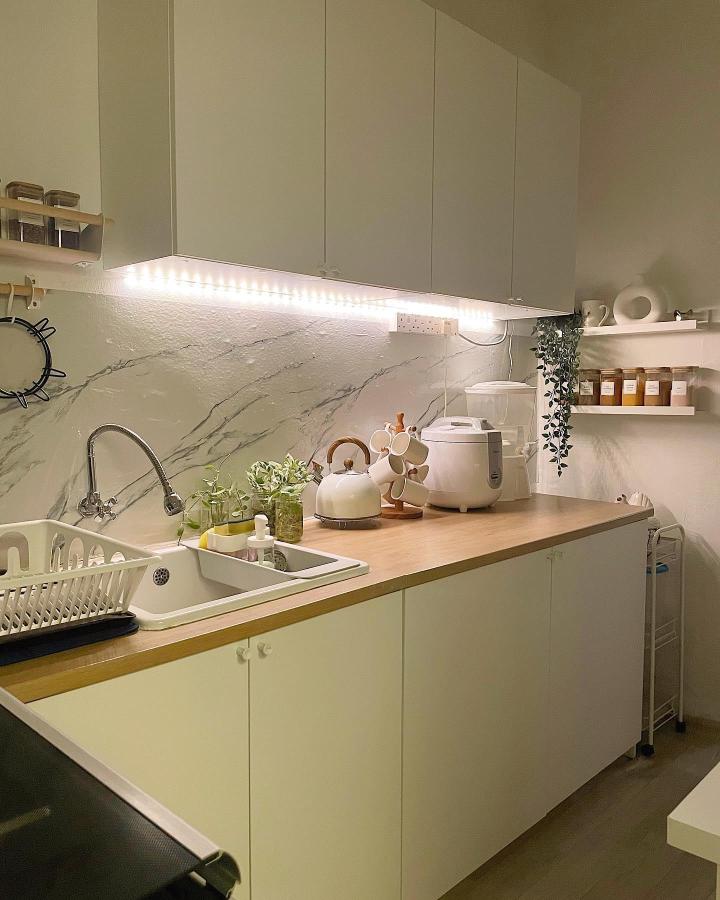 White modern kitchen with LED shelf lighting and wood countertop from @rumah.sara. Bright tidy small space with clever storage and marble backsplash.