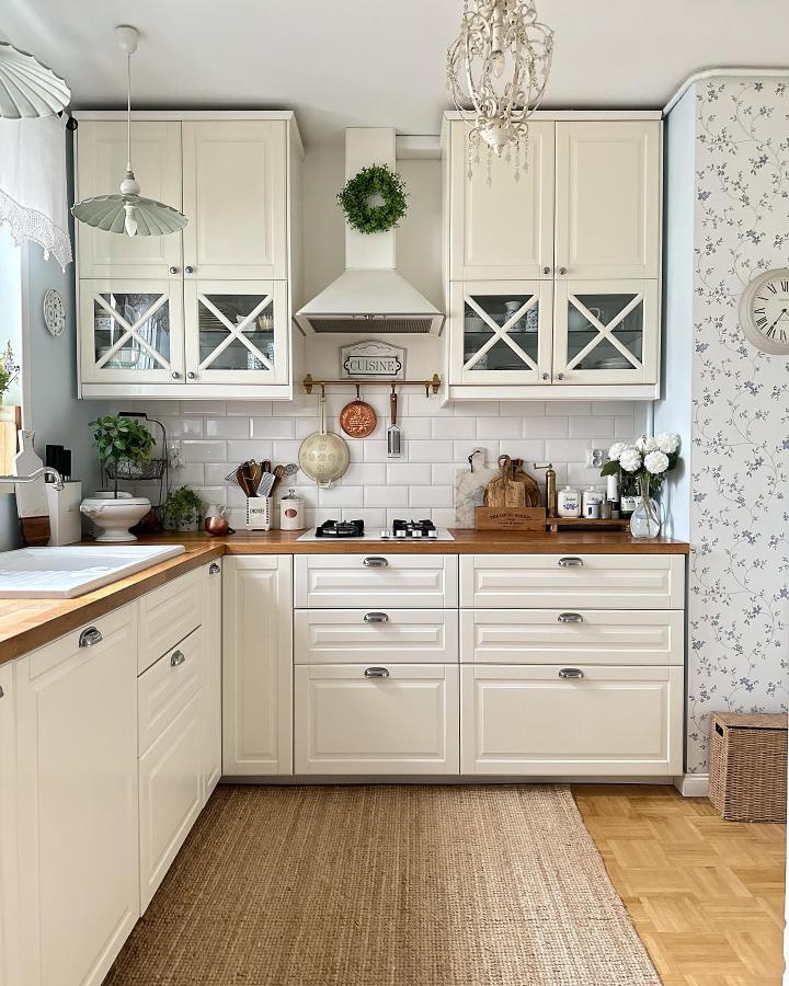 White farmhouse style kitchen with glass cabinet fronts and wood countertops from @bryczkaa featuring ikea kitchen hacks and cozy decorative details