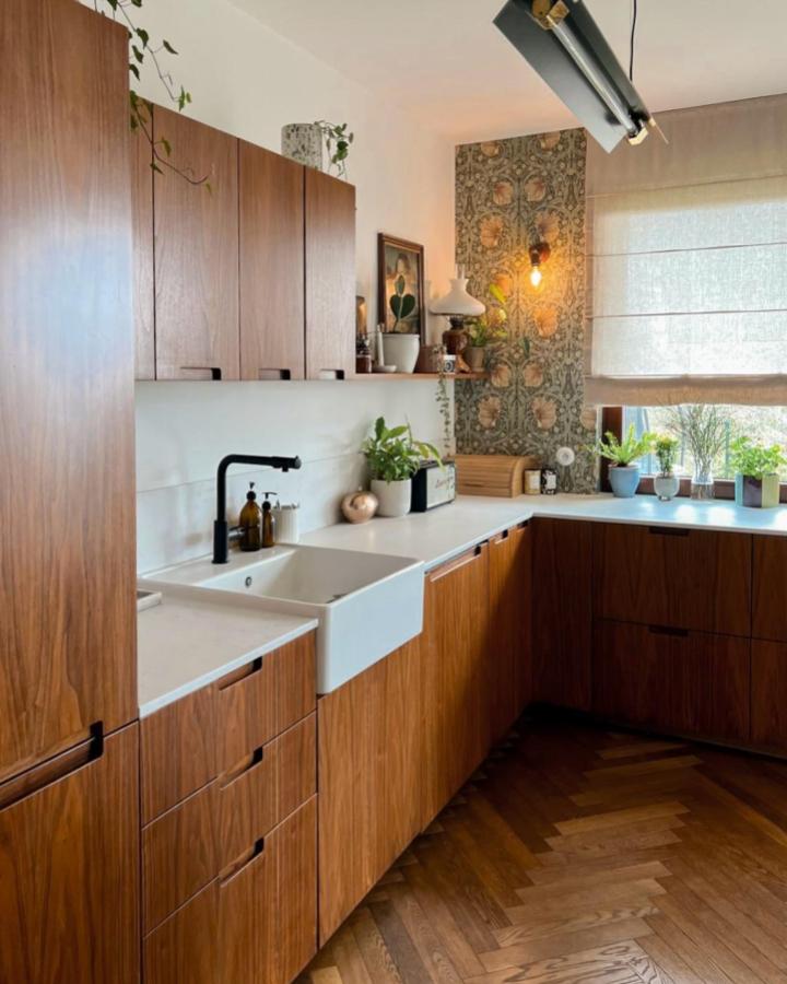 Walnut custom cabinet fronts and integrated pulls in an Ikea kitchen by @woodandpaperpl with farmhouse sink and patterned wallpaper corner.