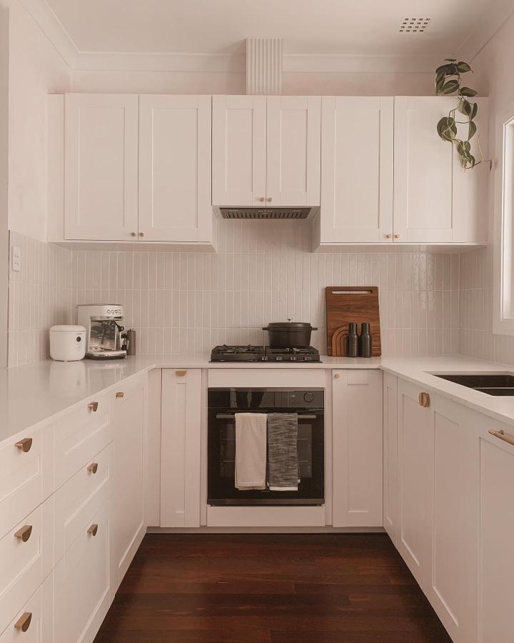 White shaker cabinets with leather handles ikea kitchen hacks by @carmenchia in a clean modern kitchen with vertical tile backsplash and dark wood floor.