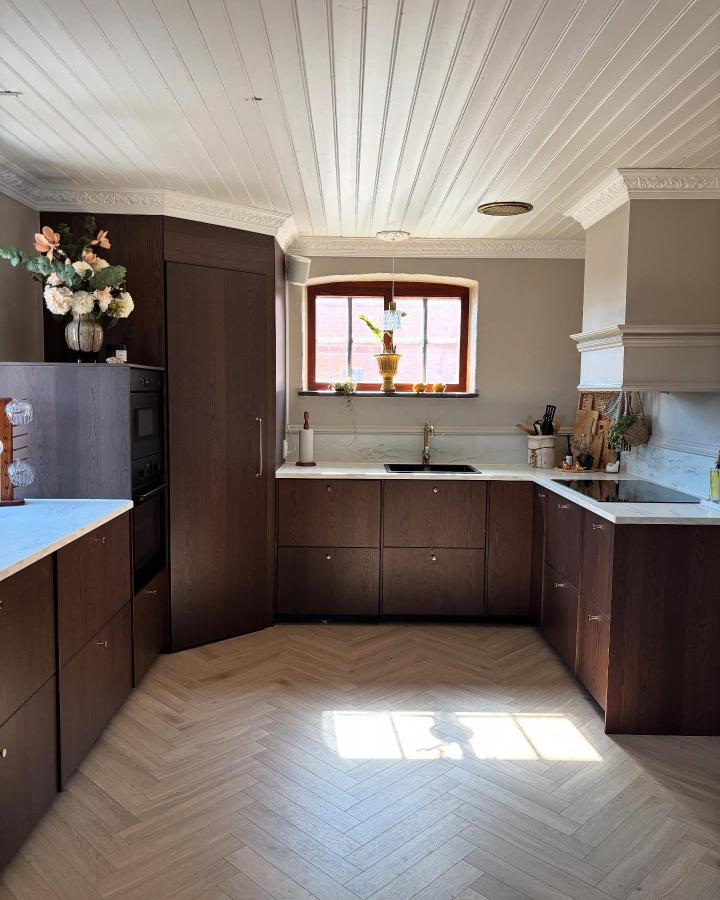 Dark wood kitchen with custom pantry and built-in range hood from @villa.bergeling. Cozy, elegant space with marble countertops and light herringbone floor.