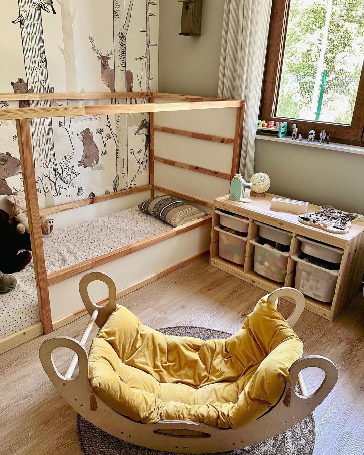 Natural wood and cream kids room with IKEA Kura bed and Trofast storage bench from @nasze_82m featuring cozy neutral tones and forest wallpaper.