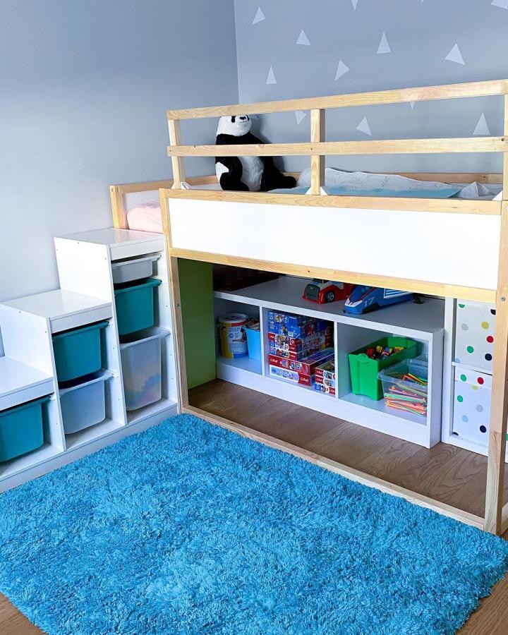 Natural wood and white Trofast storage stairs with colorful bins and organized shelves under a loft bed by @mademoiselle_zu. Bright, kid-friendly playroom design maximizing space.