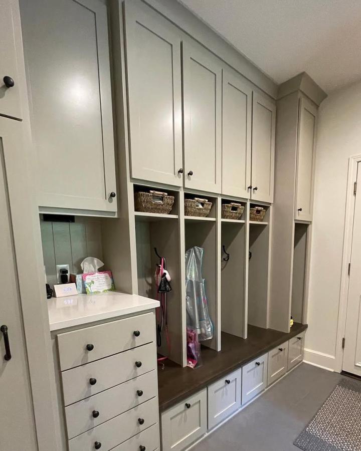 Beige custom mudroom storage with black knobs and woven baskets from @thedefineddesign. Neat cubbies with dark wood bench seating.