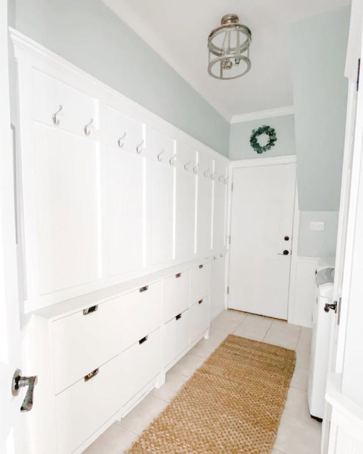White modular mudroom storage with shallow shoe bins and wall hooks by @harteandhome neat and bright hallway organization solution.