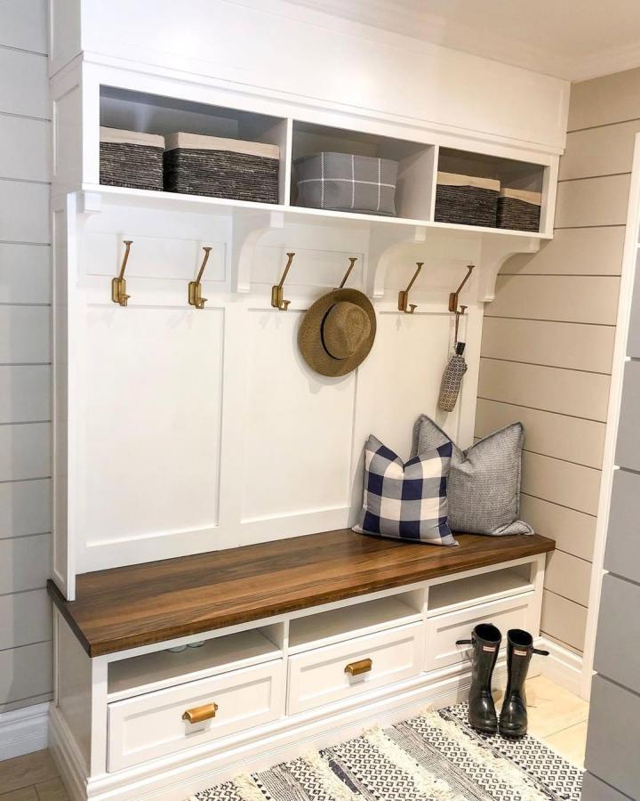 White IKEA Hemnes mudroom bench with brass hooks and storage baskets from @beaconhome_design. Cozy seating with organized compartments.