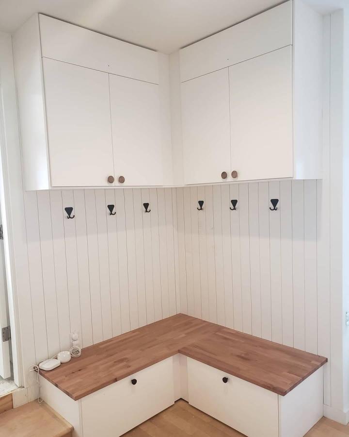 White and natural wood corner mudroom seating and storage unit with hooks by @mjlarrabeeinstaller. Clean, practical, and warm space.