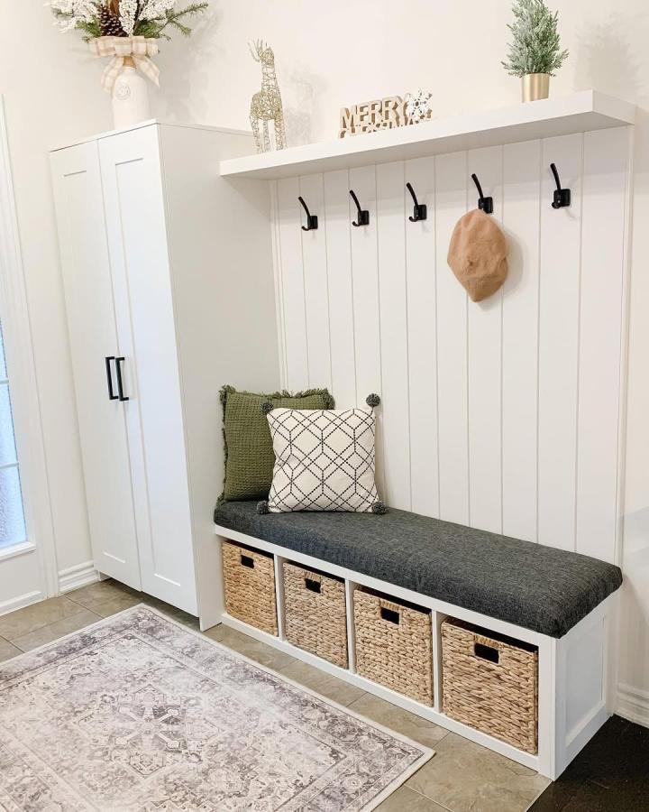 White Ikea Pax wardrobe turned storage lockers with woven baskets and dark gray bench cushion in mudroom by @designedbyshirlee. Bright, organized entryway setup.