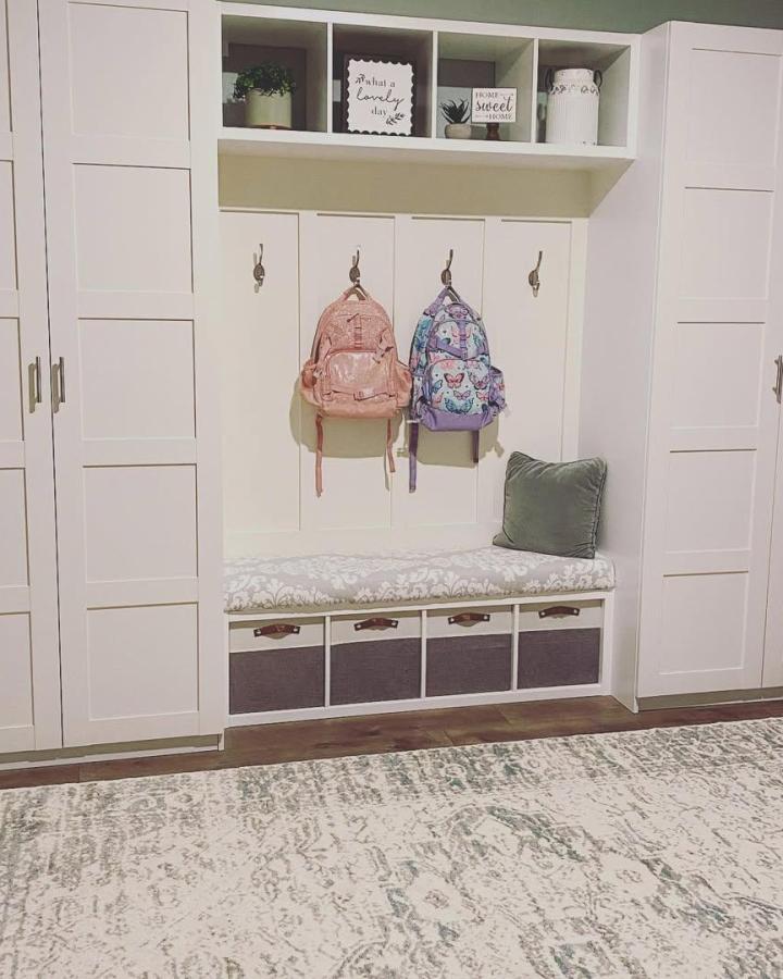 White painted mudroom seating with cubbies and hooks from @_maria_kertesz_ featuring cushioned bench and leather basket pulls for storage.